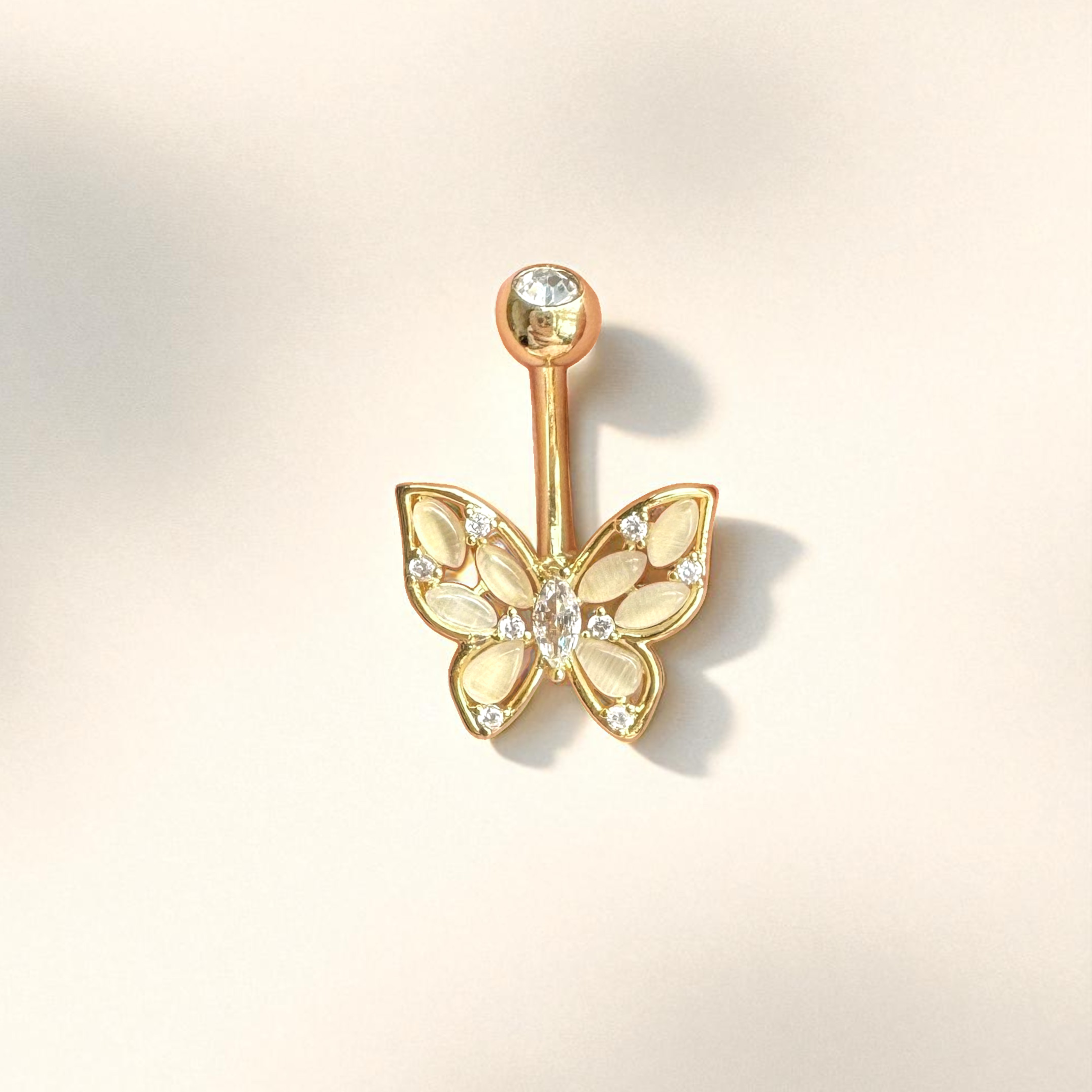 Gold butterfly-shaped belly button ring on a light beige background