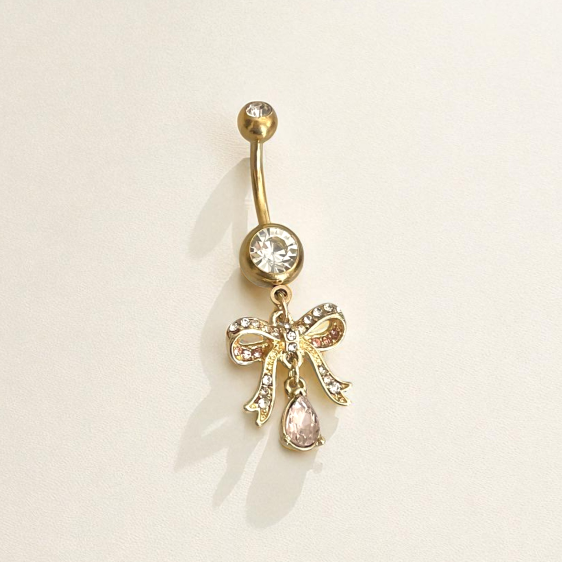 Gold belly button ring with bow and gemstone on a beige background