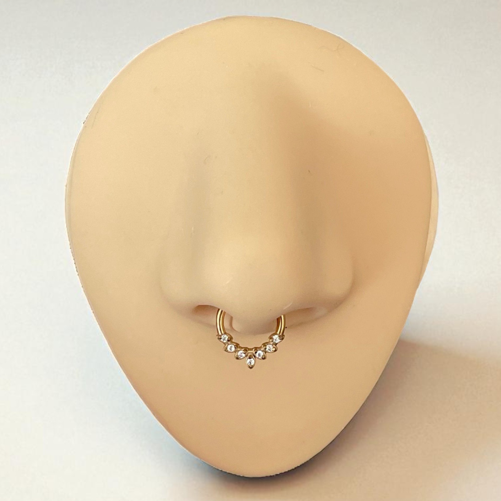 Gold nose ring with small czs on a mannequin nose against a neutral background