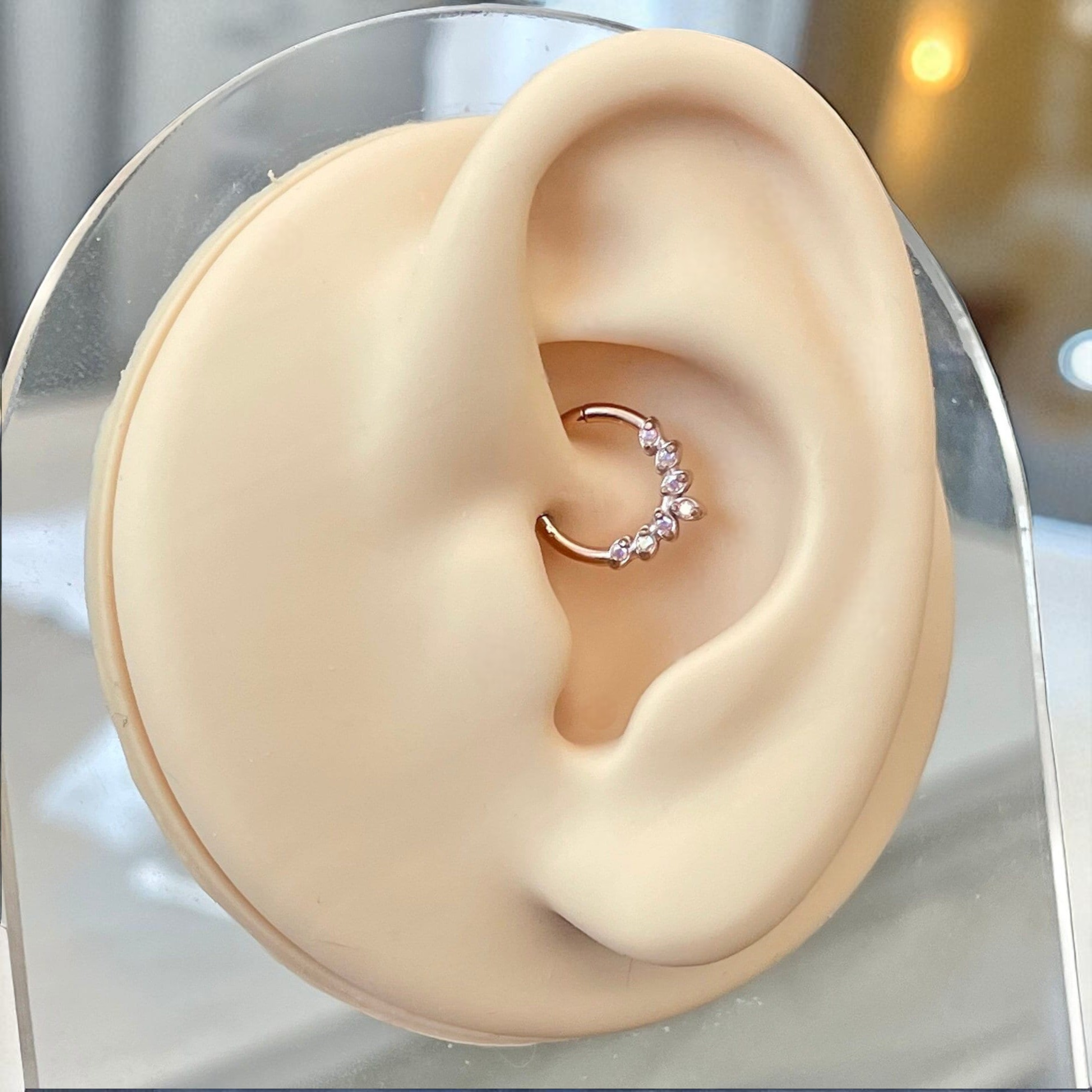Close-up of an ear wearing a rose gold earring with small stones on a clear stand.