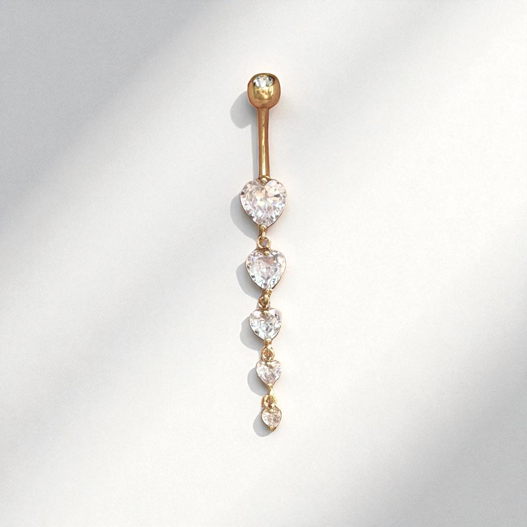 Gold belly button ring with heart-shaped gemstones on a light gray background