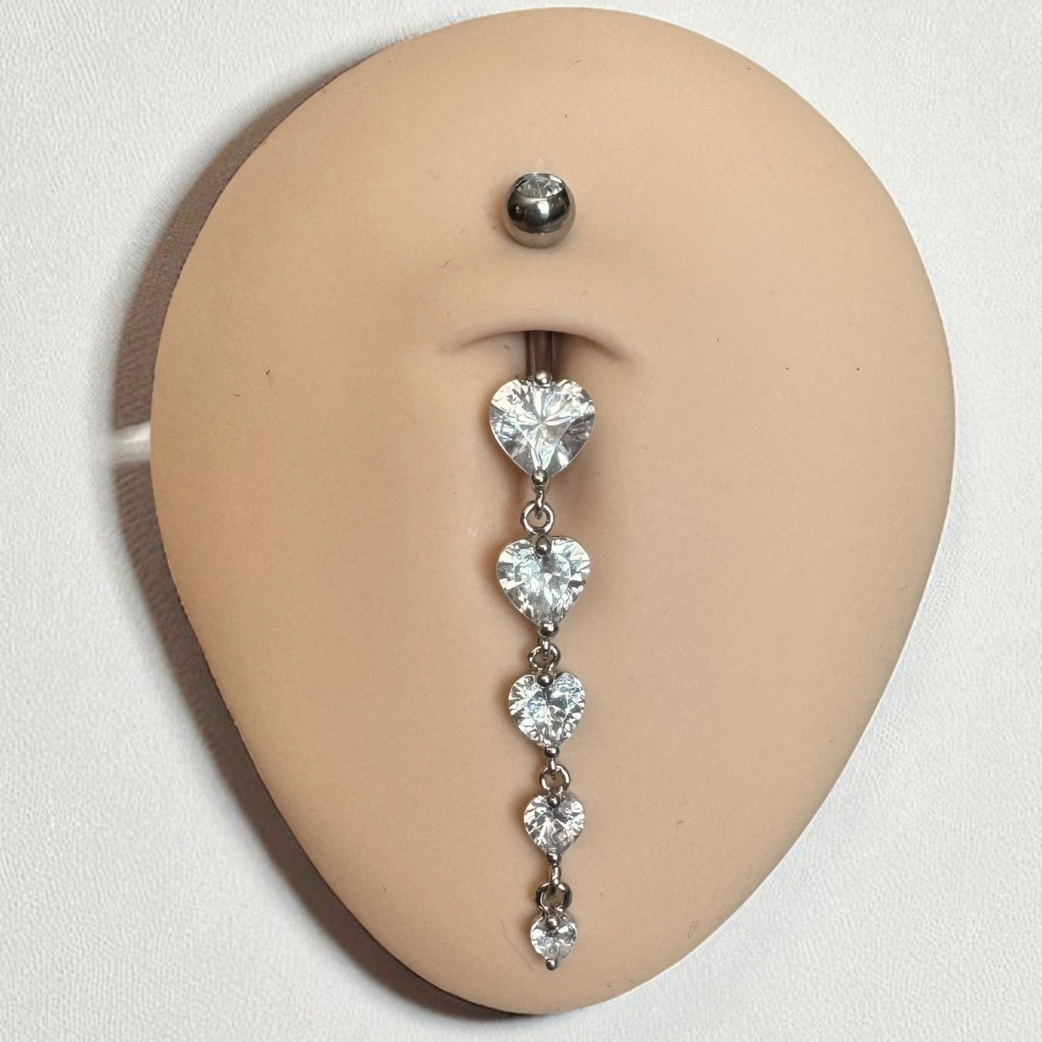 Belly button ring with heart-shaped gemstones on a beige model background