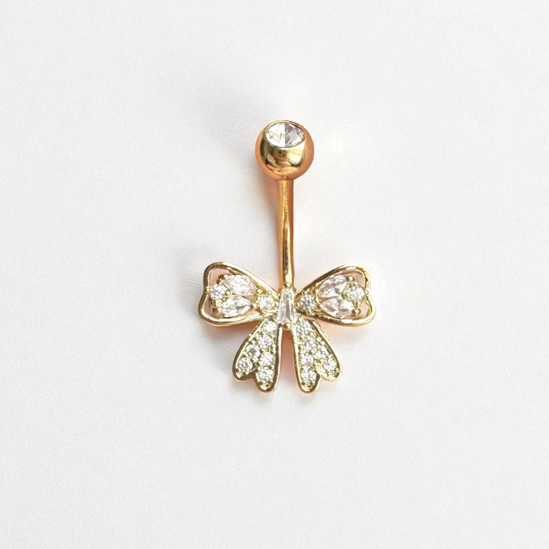 Gold belly button ring with bow design on a white background