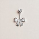 Silver bow-shaped belly button ring with clear gemstones on a light beige background