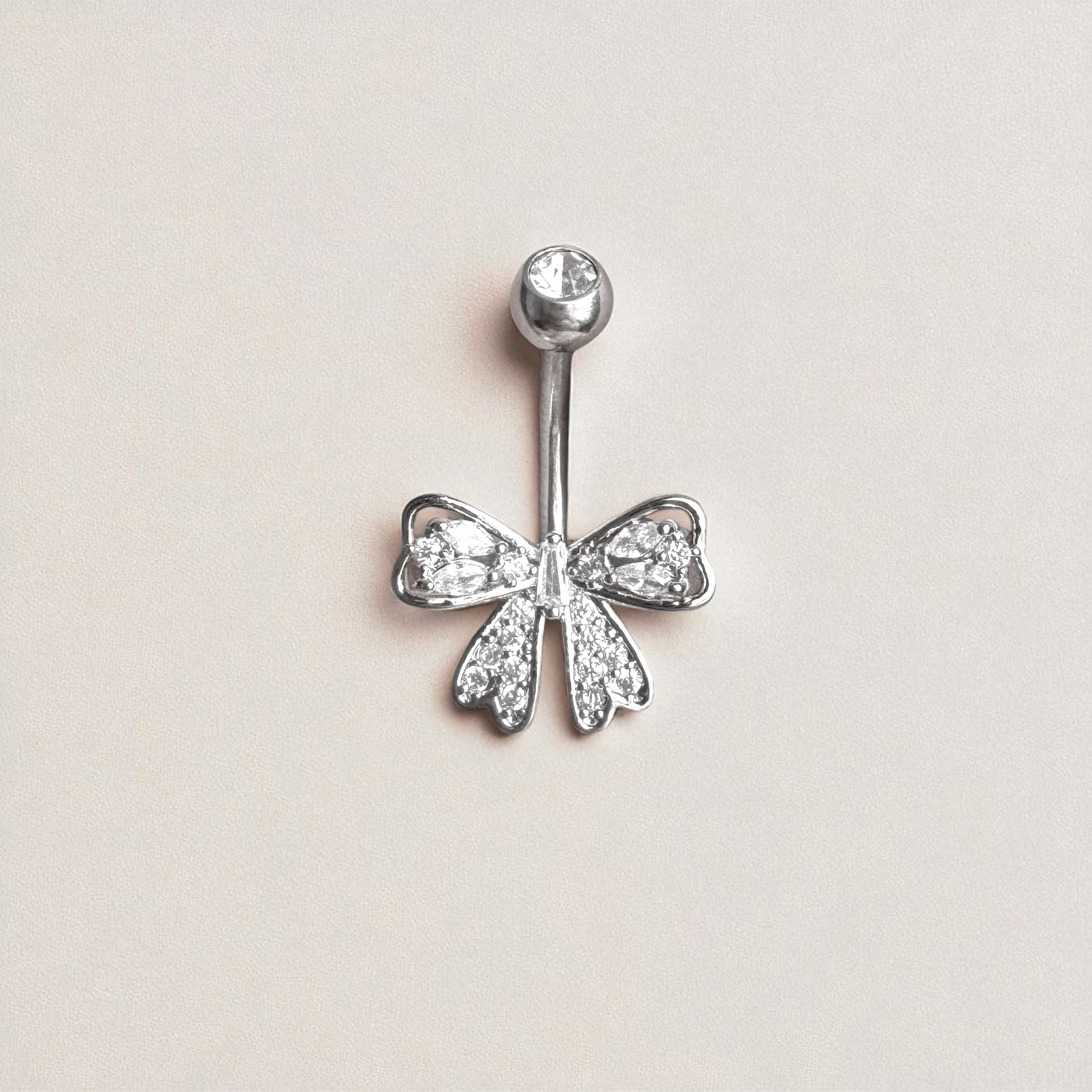Silver bow-shaped belly button ring with clear gemstones on a light beige background