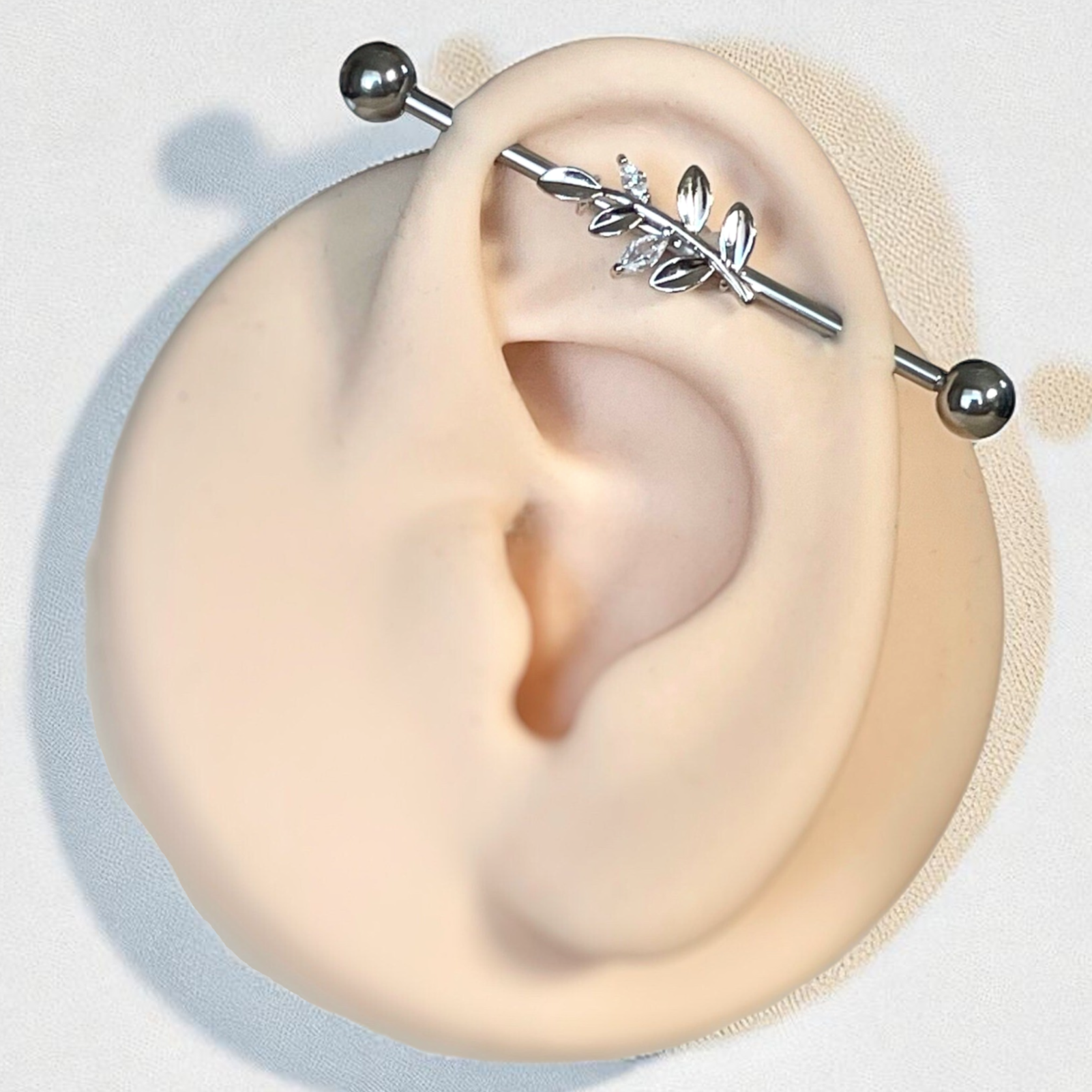 Close-up of an ear with a silver industrial earring on a light gray background