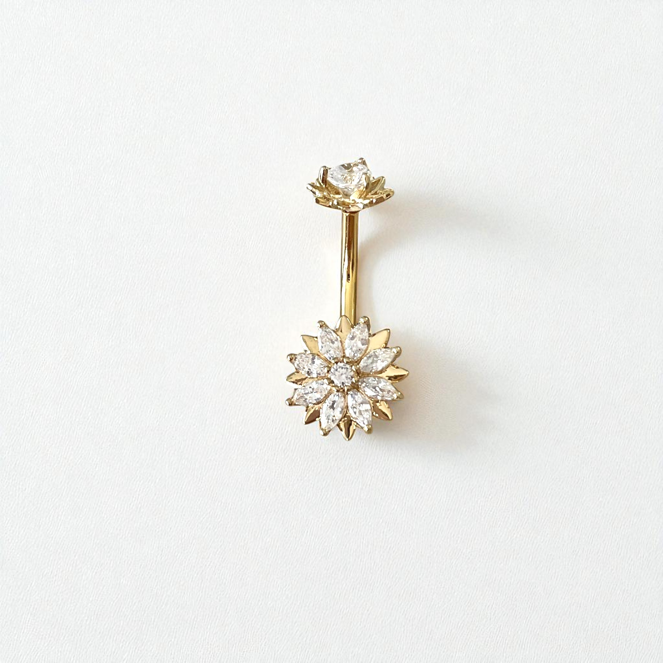 Gold belly button ring with a flower clear gem centerpiece on a white background