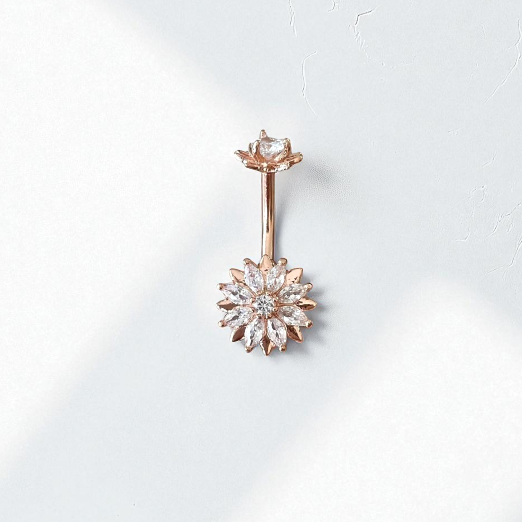 Rose gold belly button ring with clear gemstones in a flower design
on a white background
