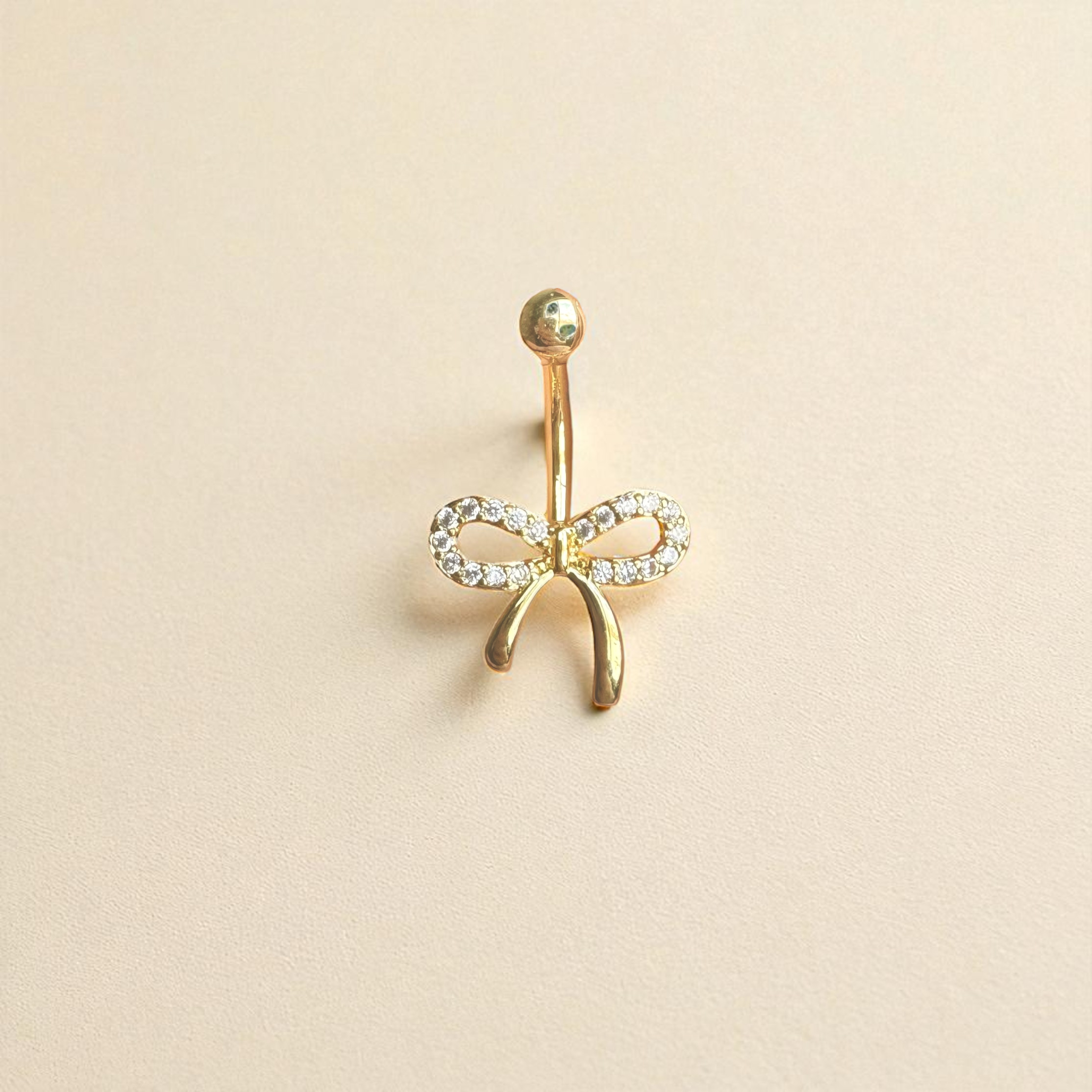 Gold bow-shaped earring with clear stones on a beige background