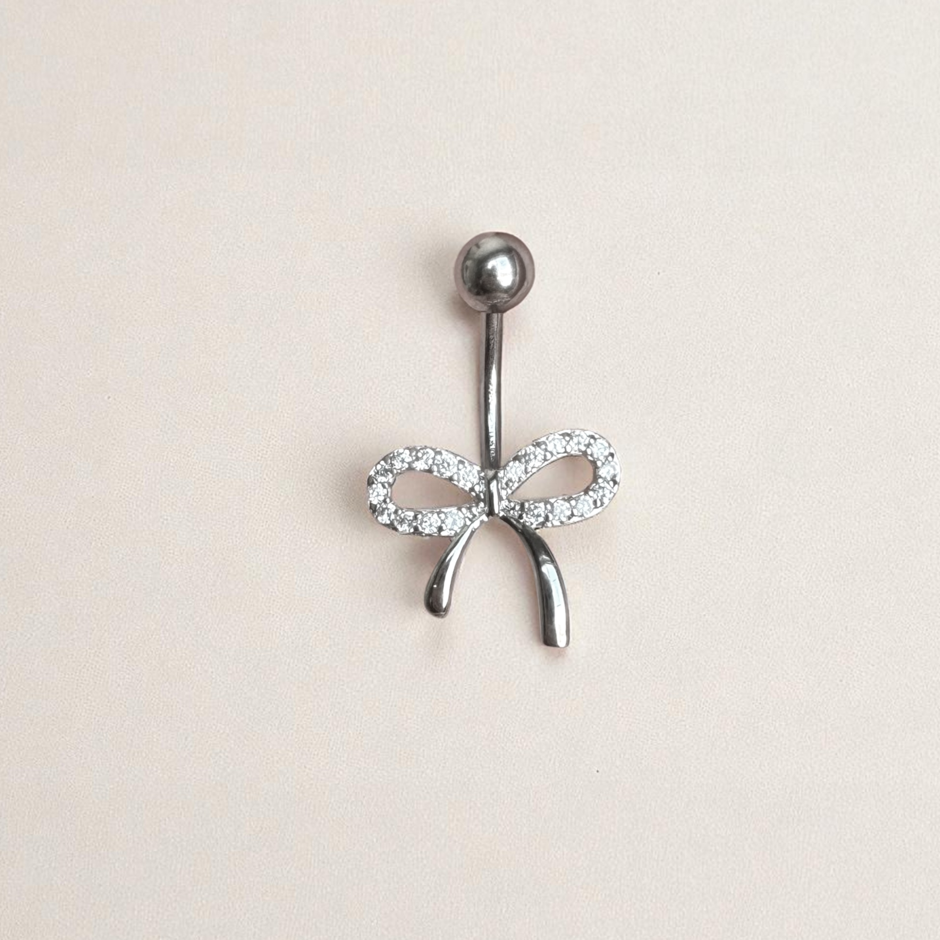 Belly button ring with bow design on a beige background