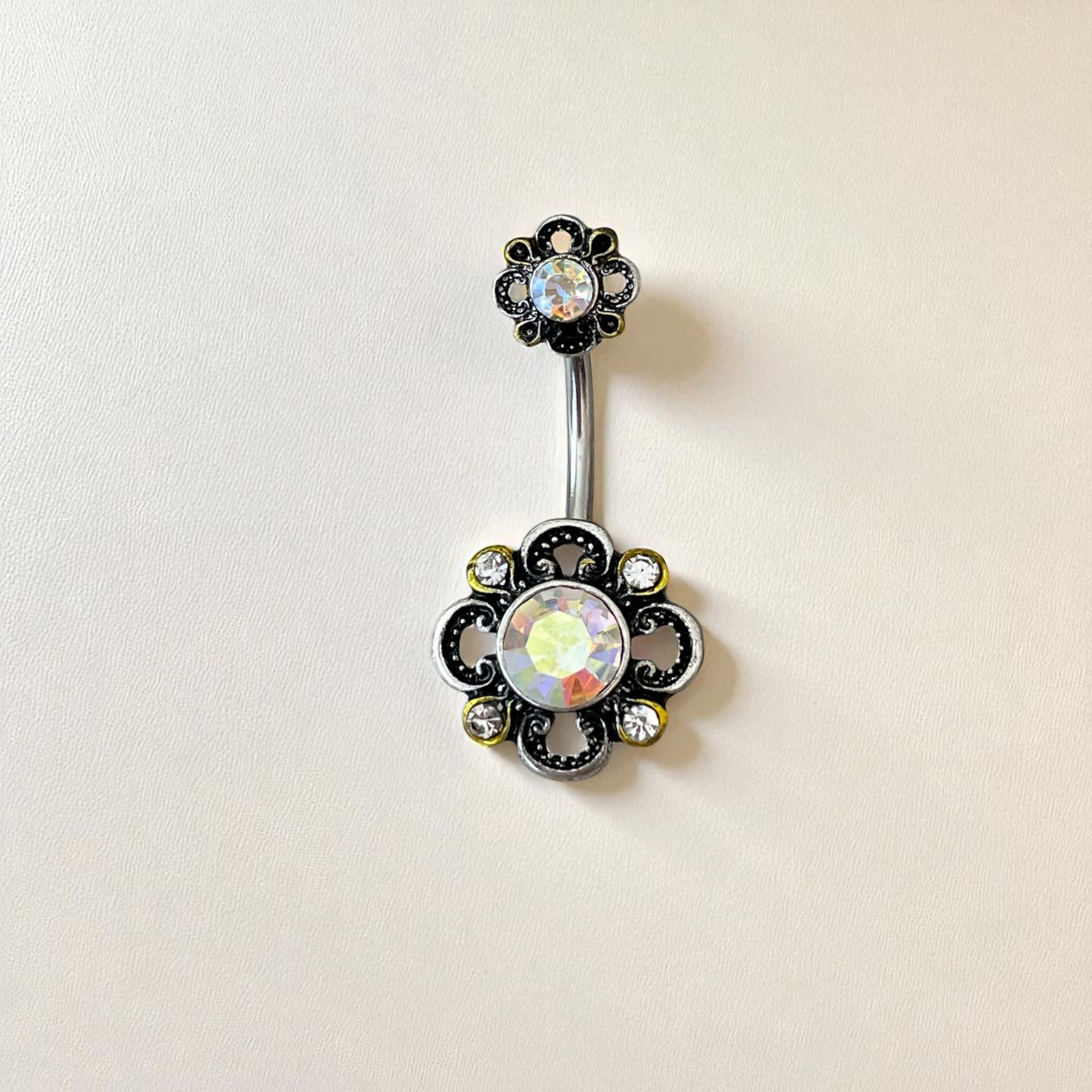 Belly button ring with floral design and gemstones on a beige background