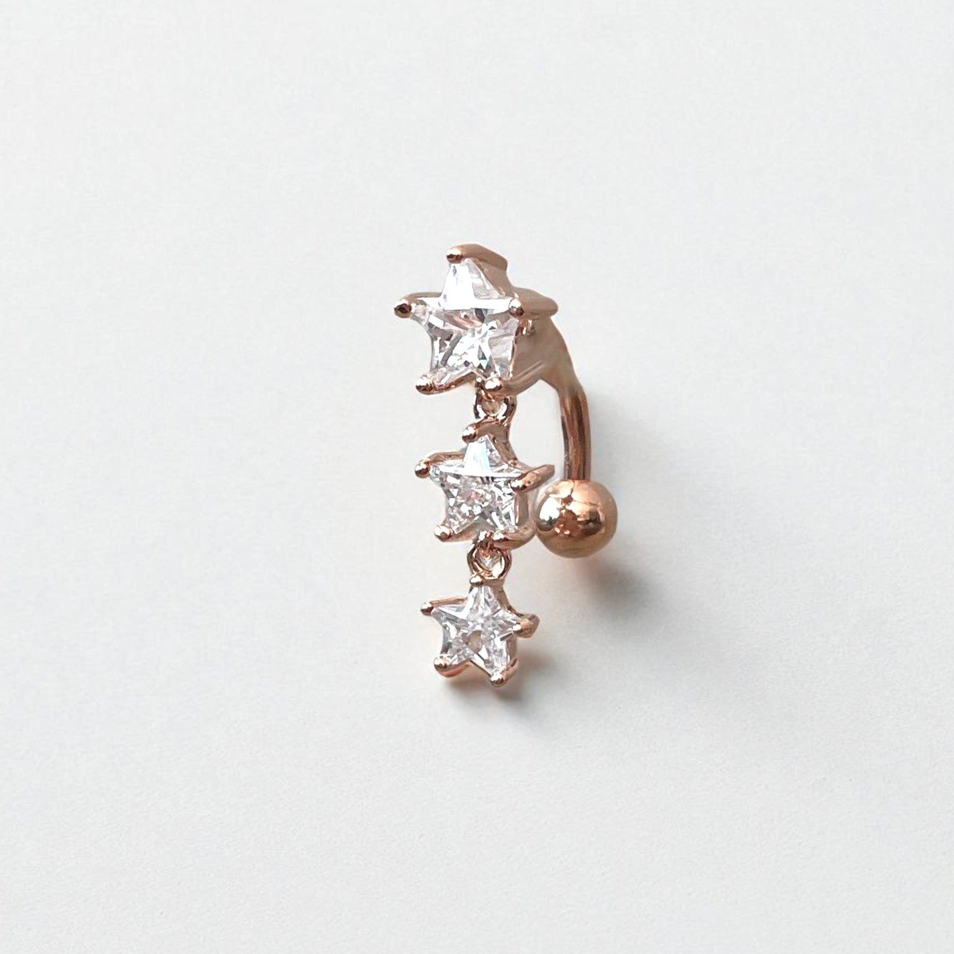 Rose gold belly button ring with clear star shaped gemstones on a light gray background