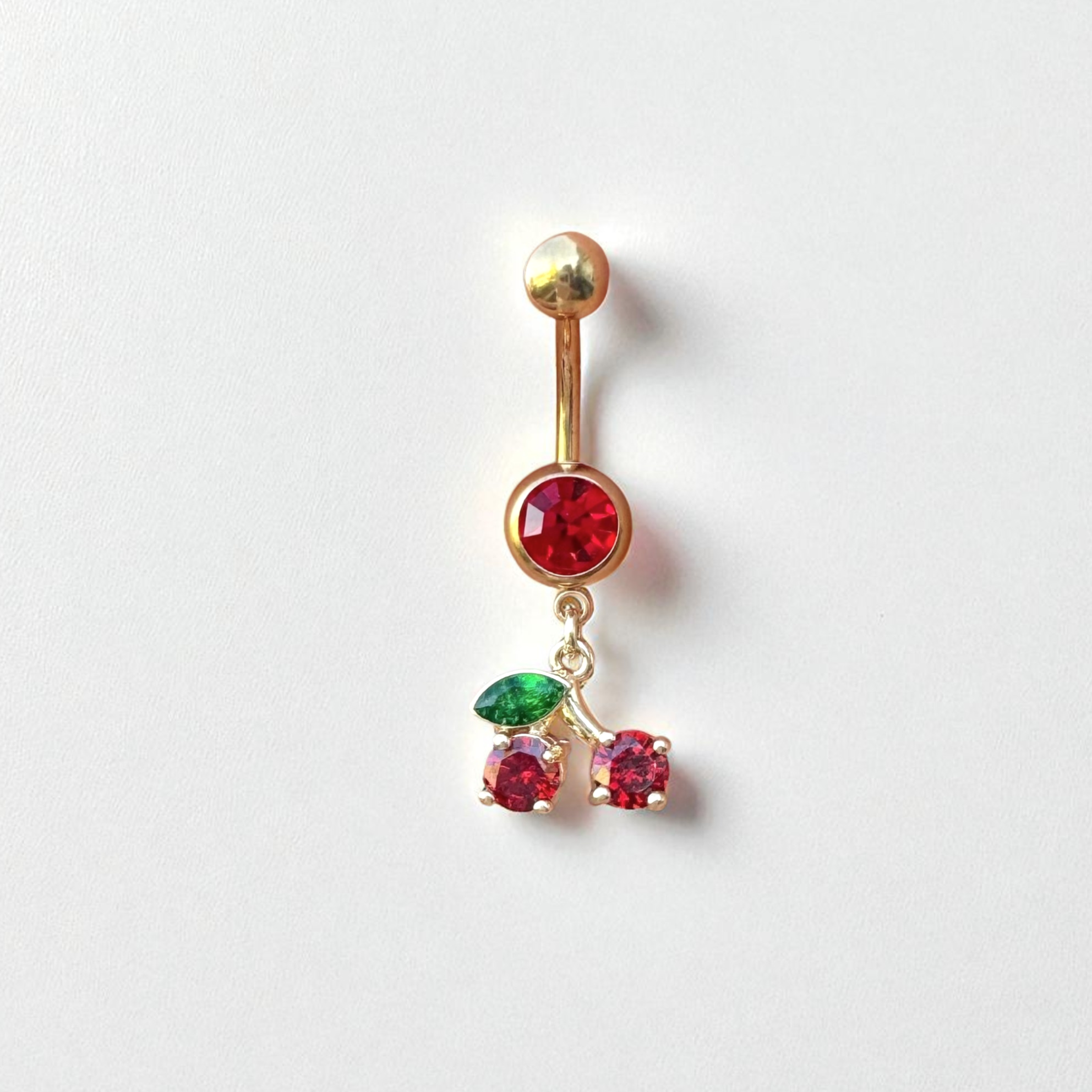 Gold belly button ring with red and green gemstones with a cherry charm on a white background