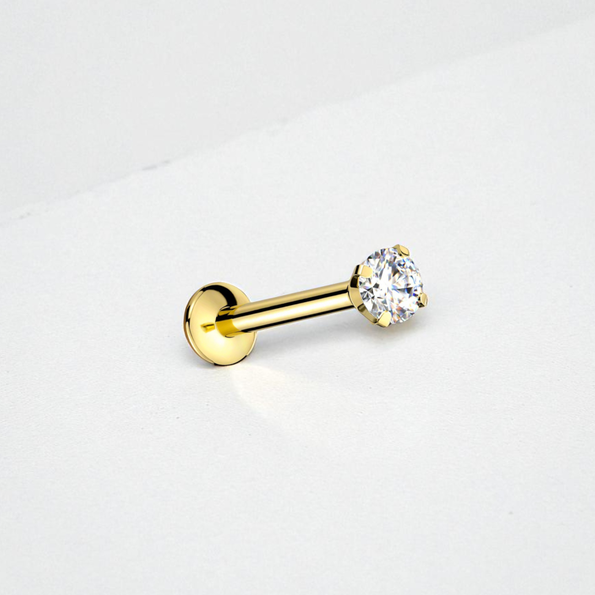 Gold flat back earring with a clear gemstone on a light gray background