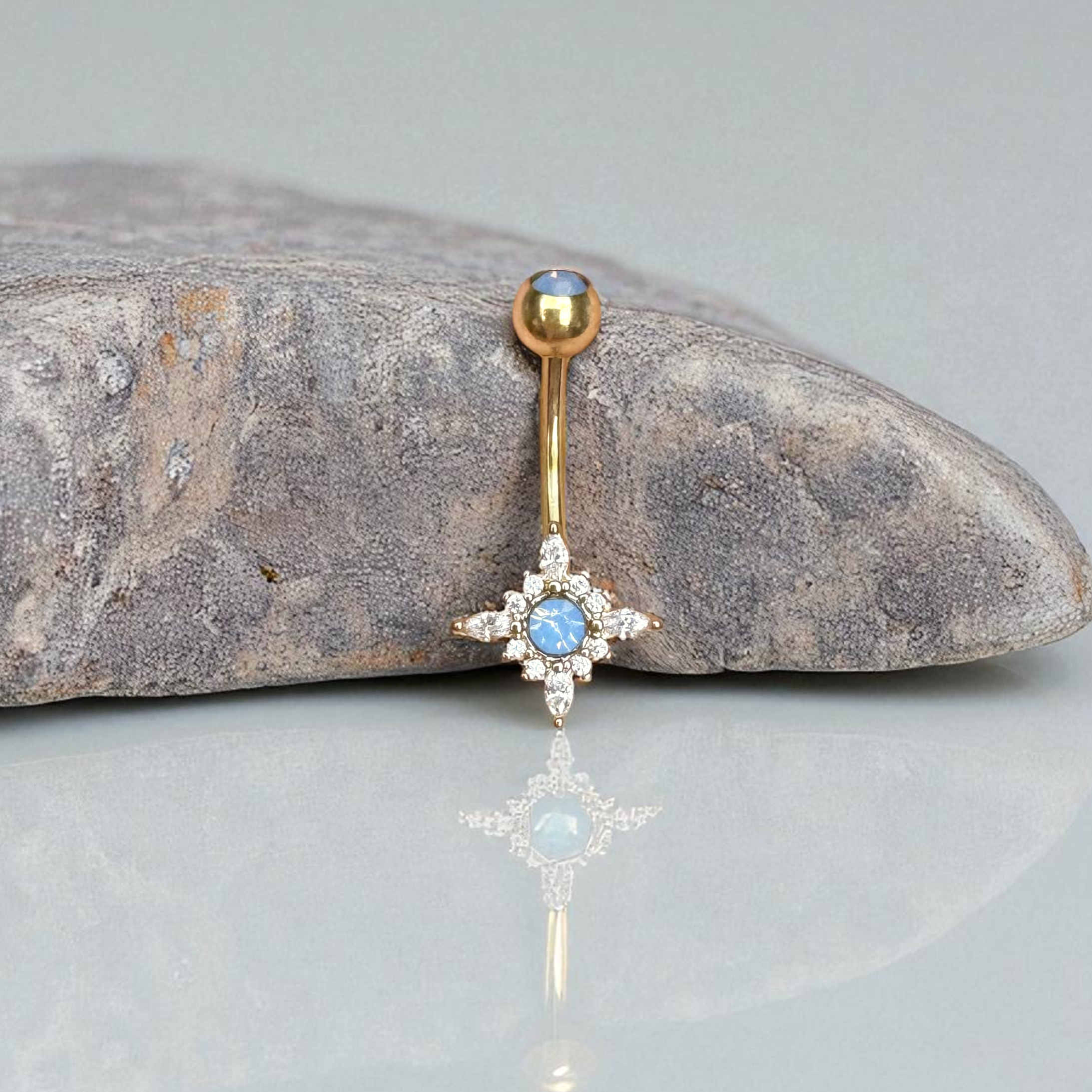 Gold belly button ring with blue gemstone on a stone surface