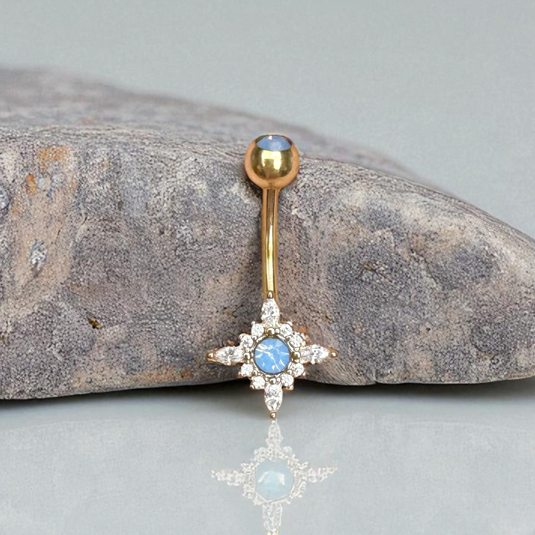 Gold belly button ring with blue gemstone on a stone surface