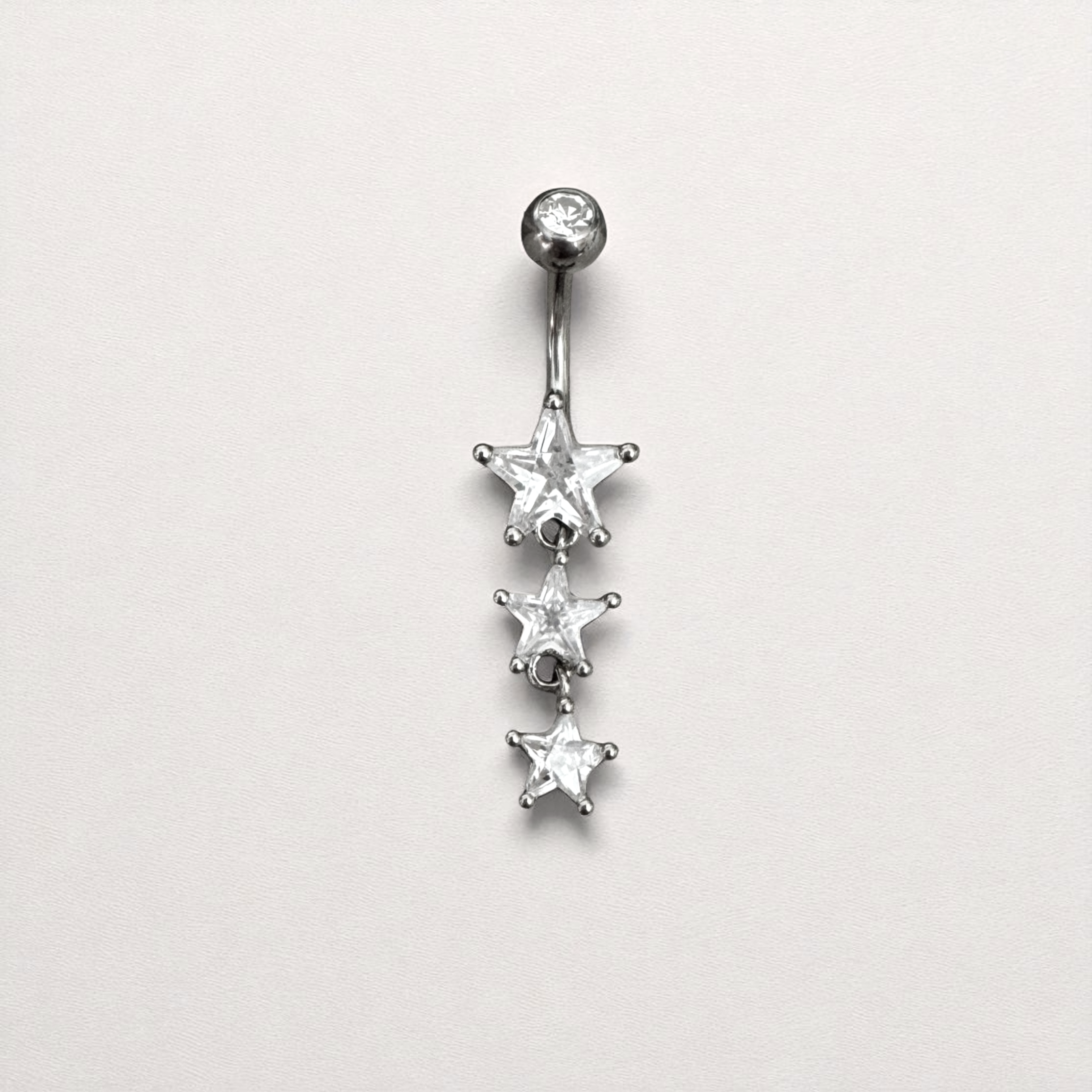 Silver belly button ring with three star-shaped gemstones on a light gray background