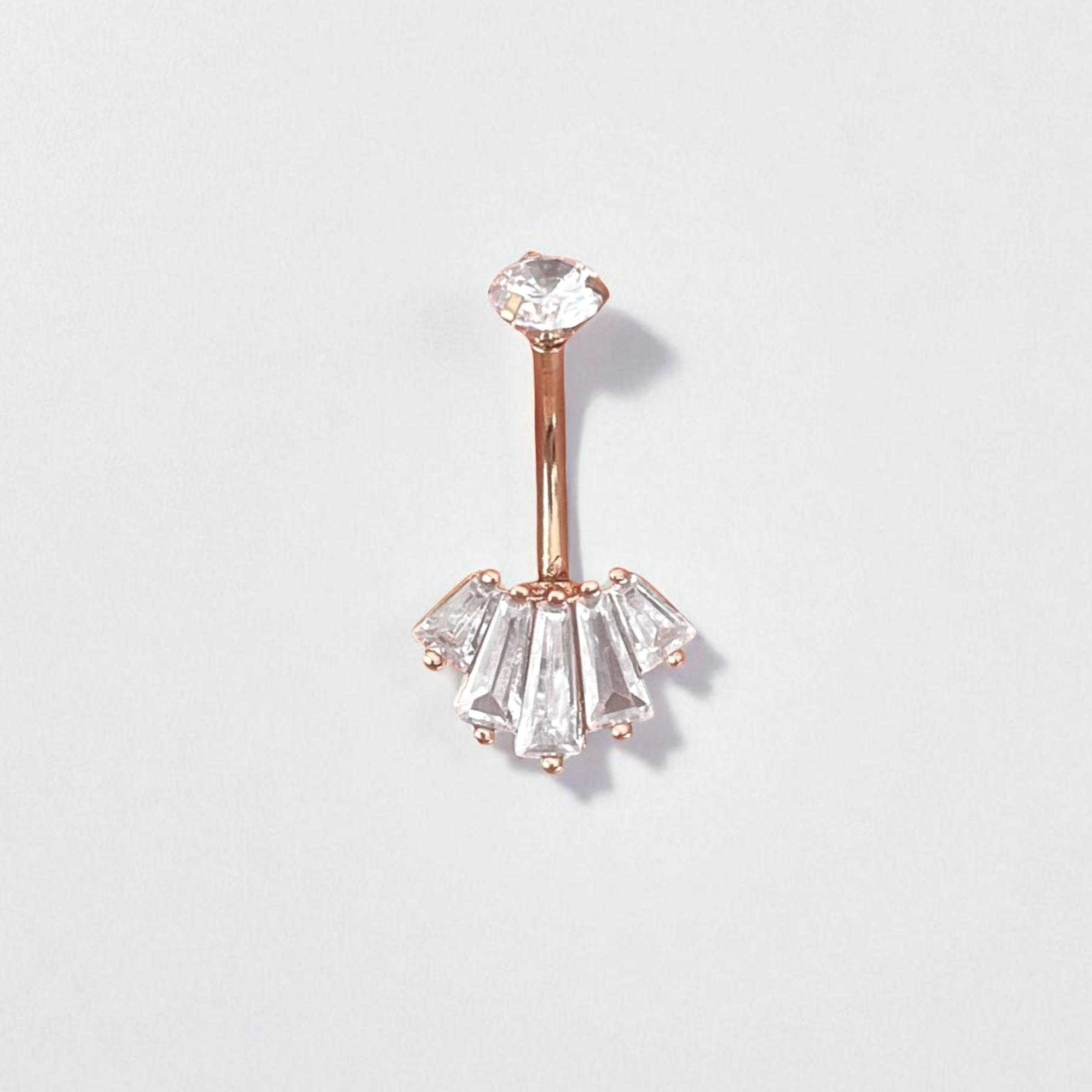 Rose gold belly button ring with clear gemstones on a light gray background