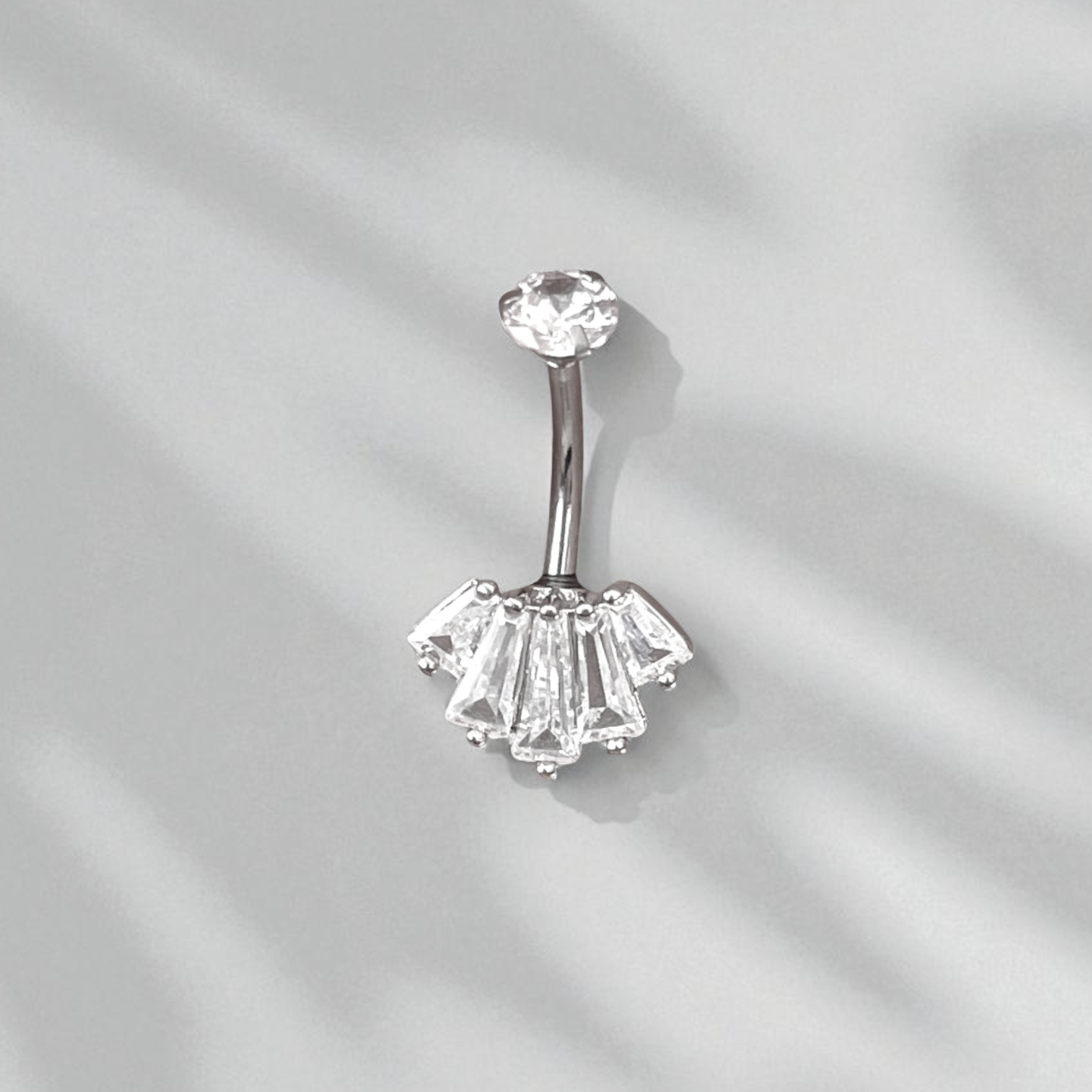 Silver belly button ring with clear gemstones on a light gray background