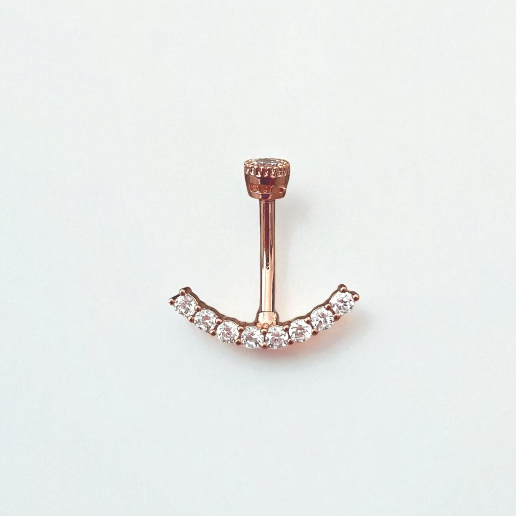 Rose gold belly button ring with clear gemstones on a light gray background