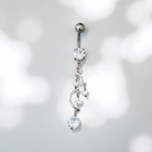 Silver belly button ring with clear gemstones on a light gray background