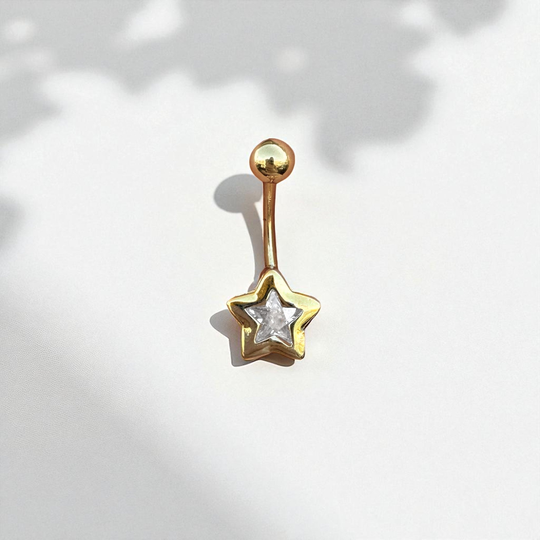 Gold star-shaped belly button ring on a light background