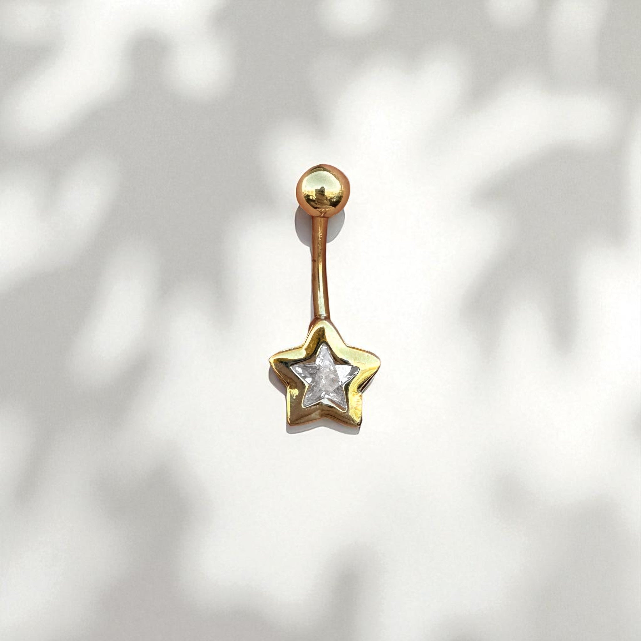 Gold star-shaped belly button ring on a white background
