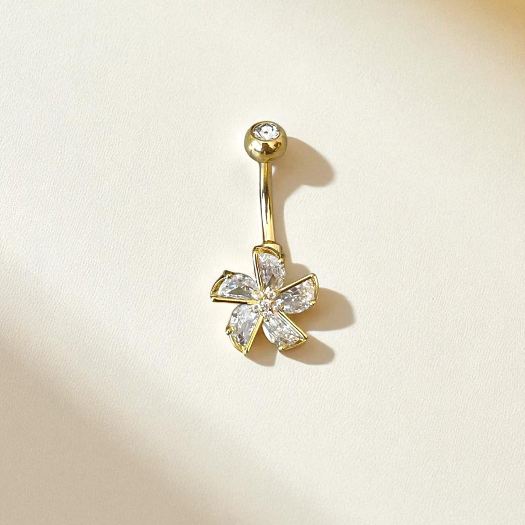 Gold belly button ring with a floral design on a beige background