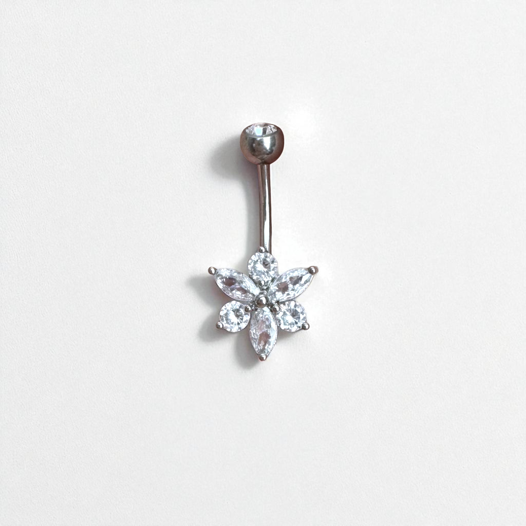 Belly button ring with a floral-shaped gem design on a light gray background