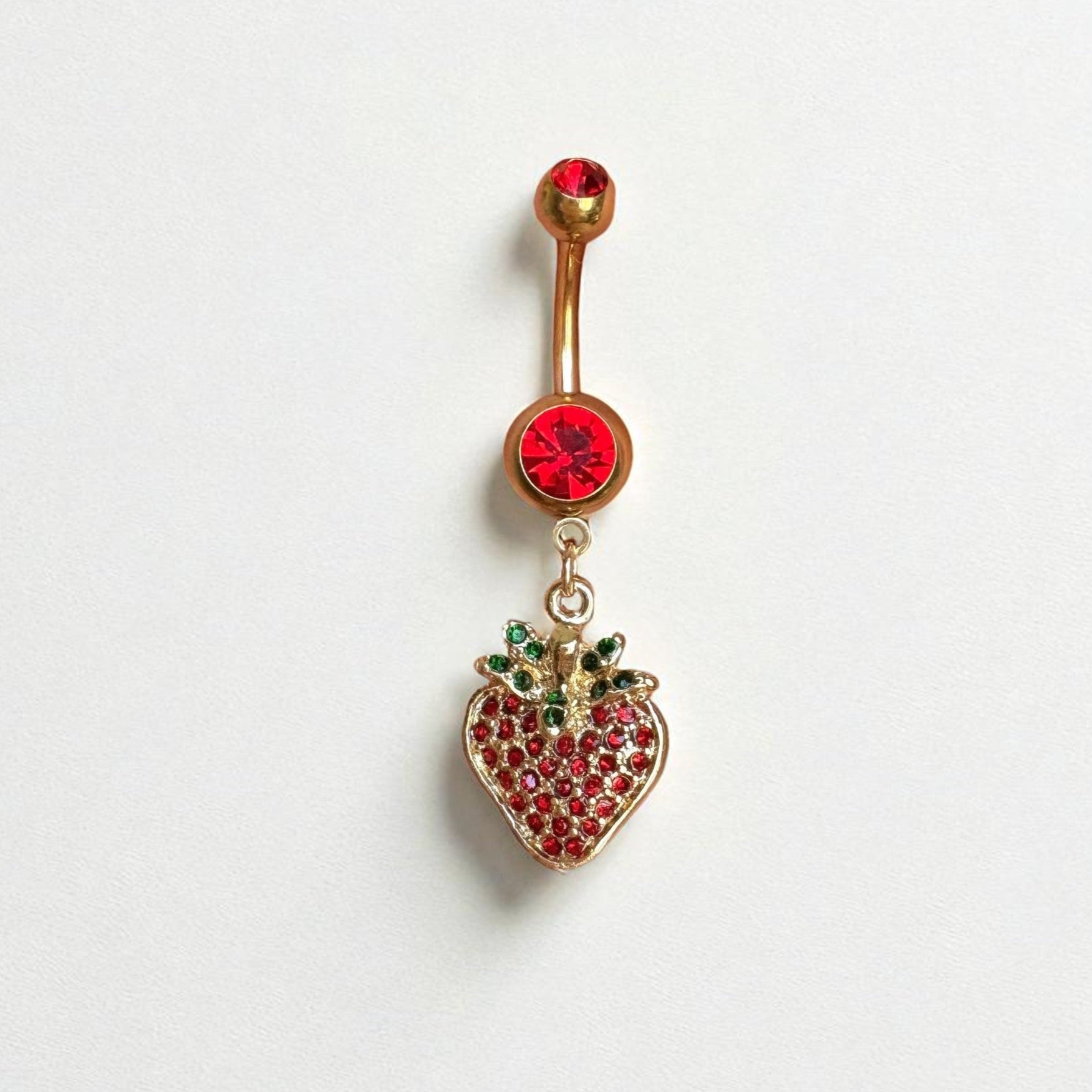 Gold belly button ring with a strawberry charm with red and green gemstones on a white background