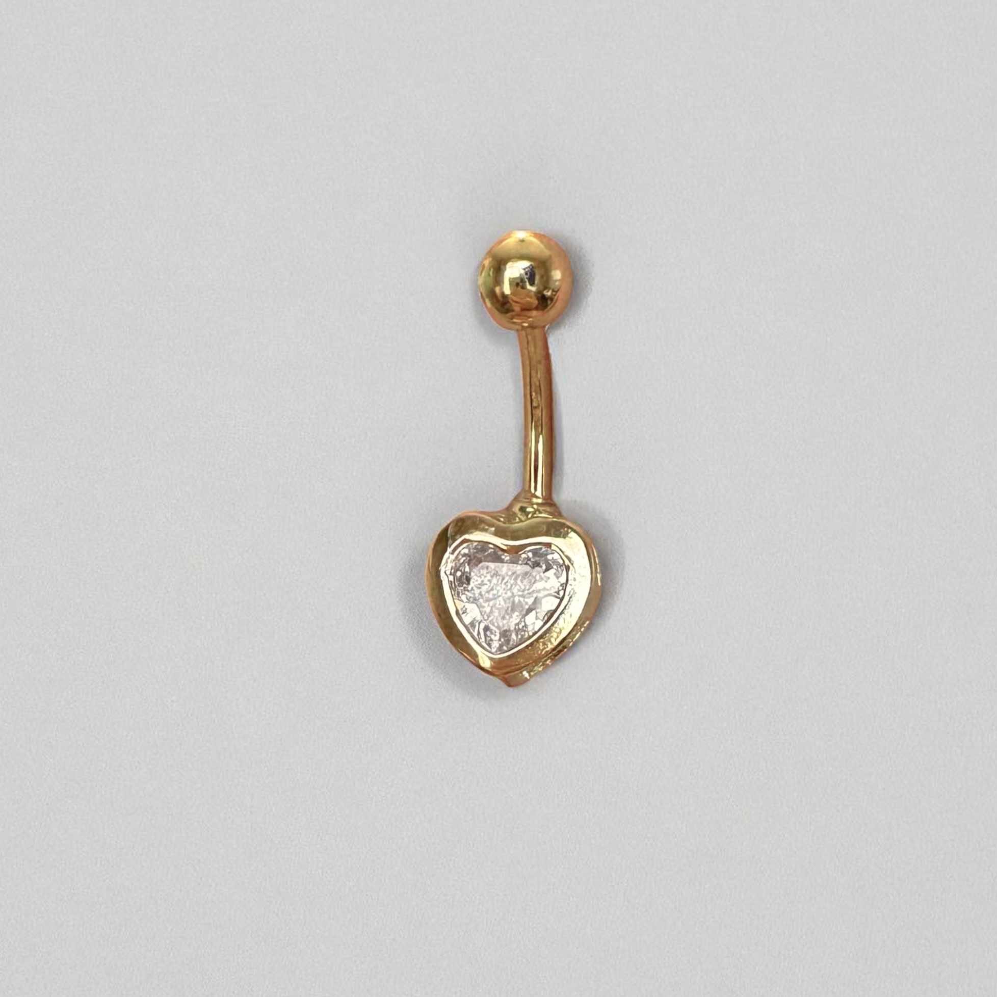Gold belly button ring with heart-shaped CZ on a gray background