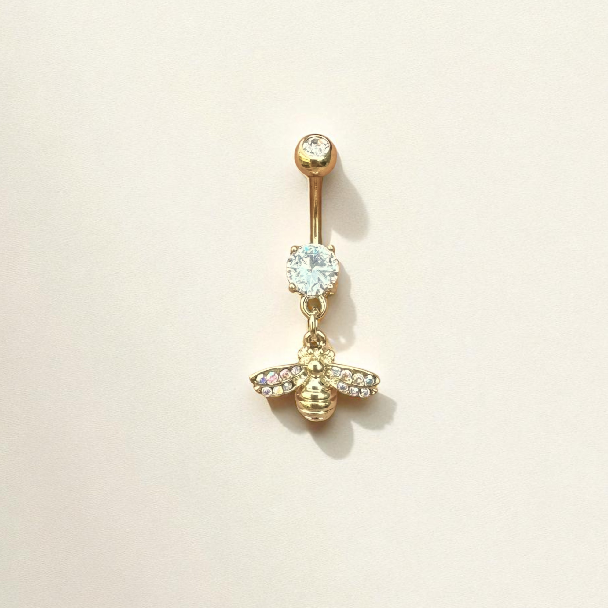 Gold belly button ring with bee and gemstone design on a beige background