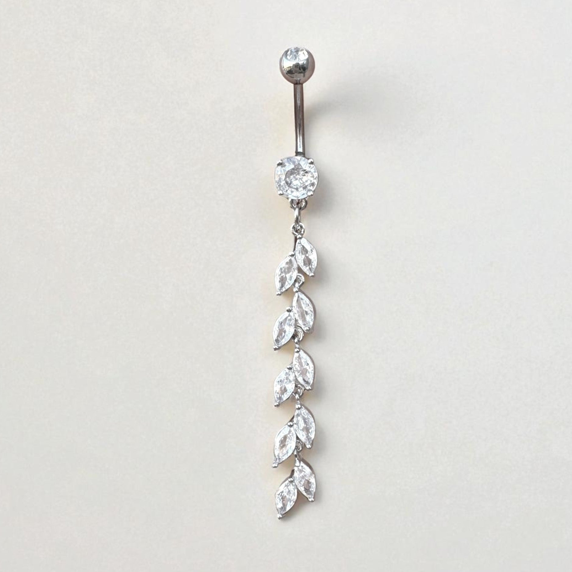 Silver belly button ring with clear gemstones on a light gray background