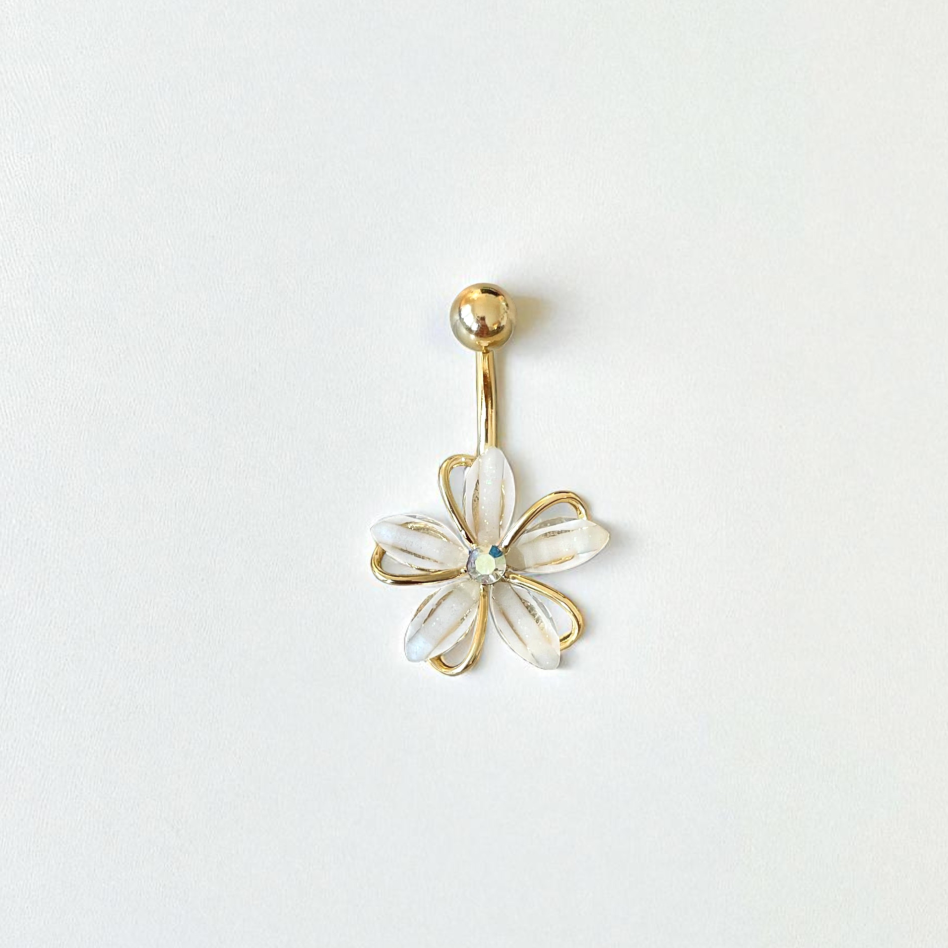 Gold belly button ring with a white flower design on a light gray background