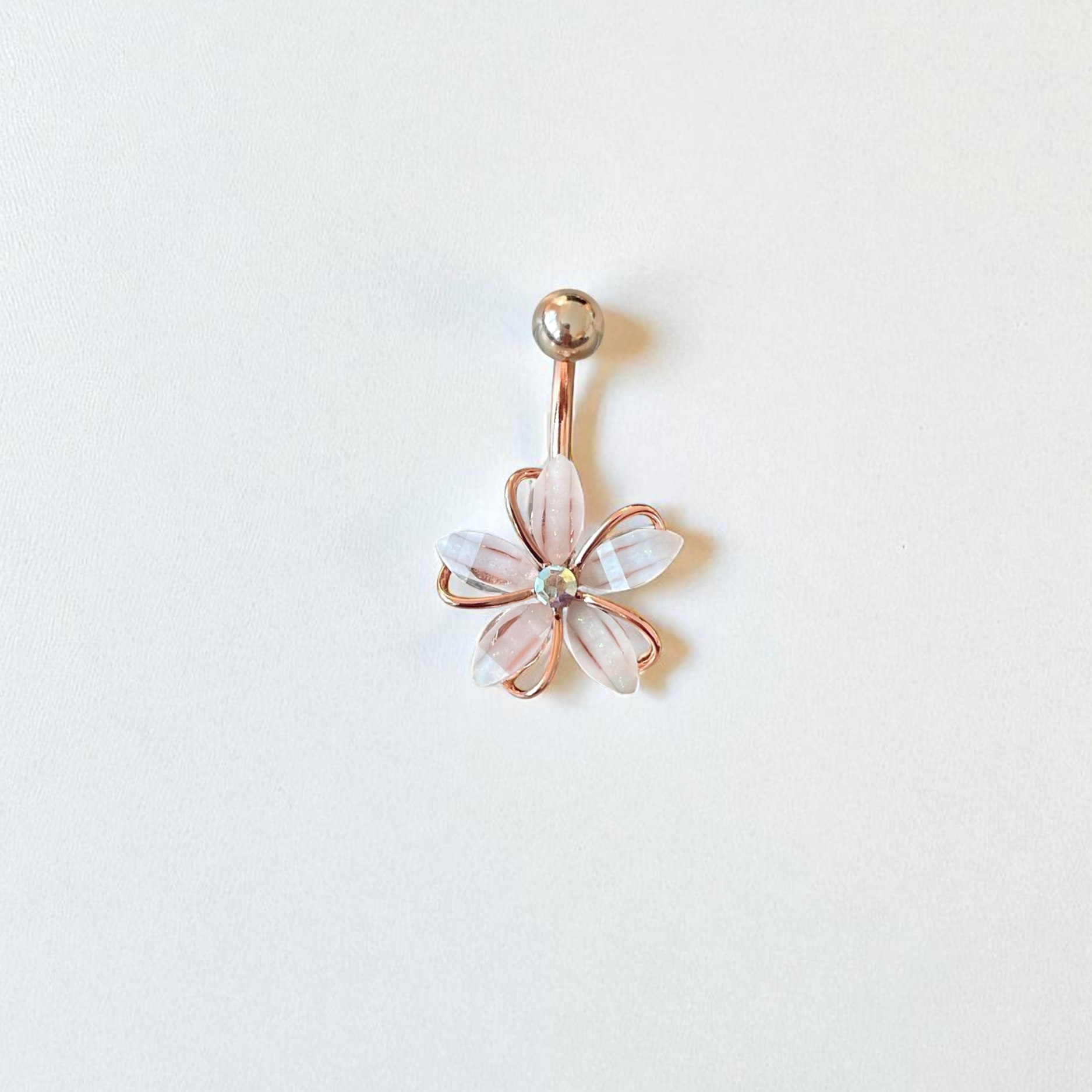 Rose gold belly button ring with a floral design on a white background