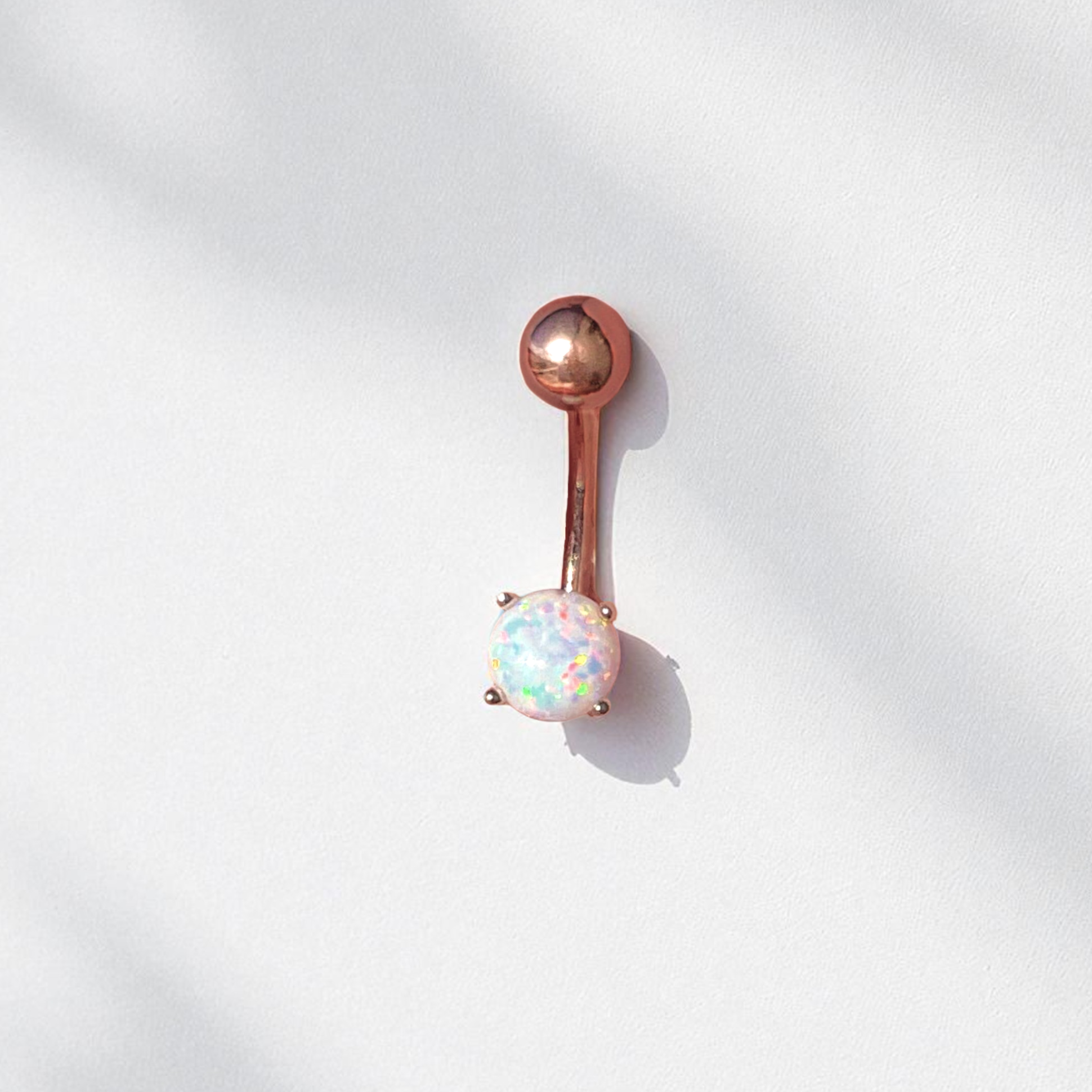 Rose gold belly button ring with an opal gemstone on a white background
