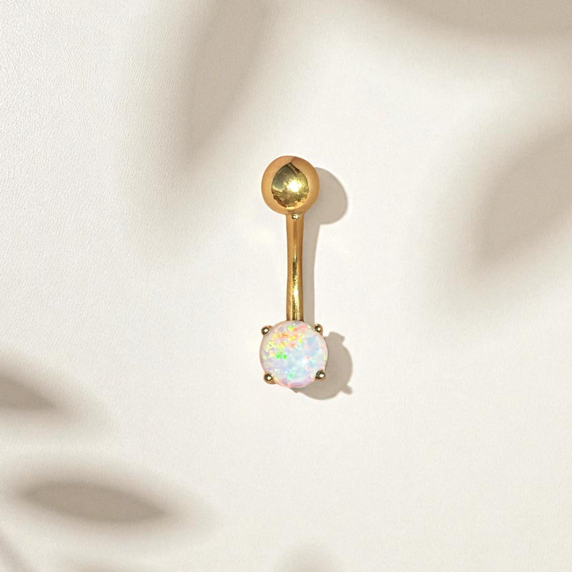Gold belly button ring with a white opal stone on a beige fabric background