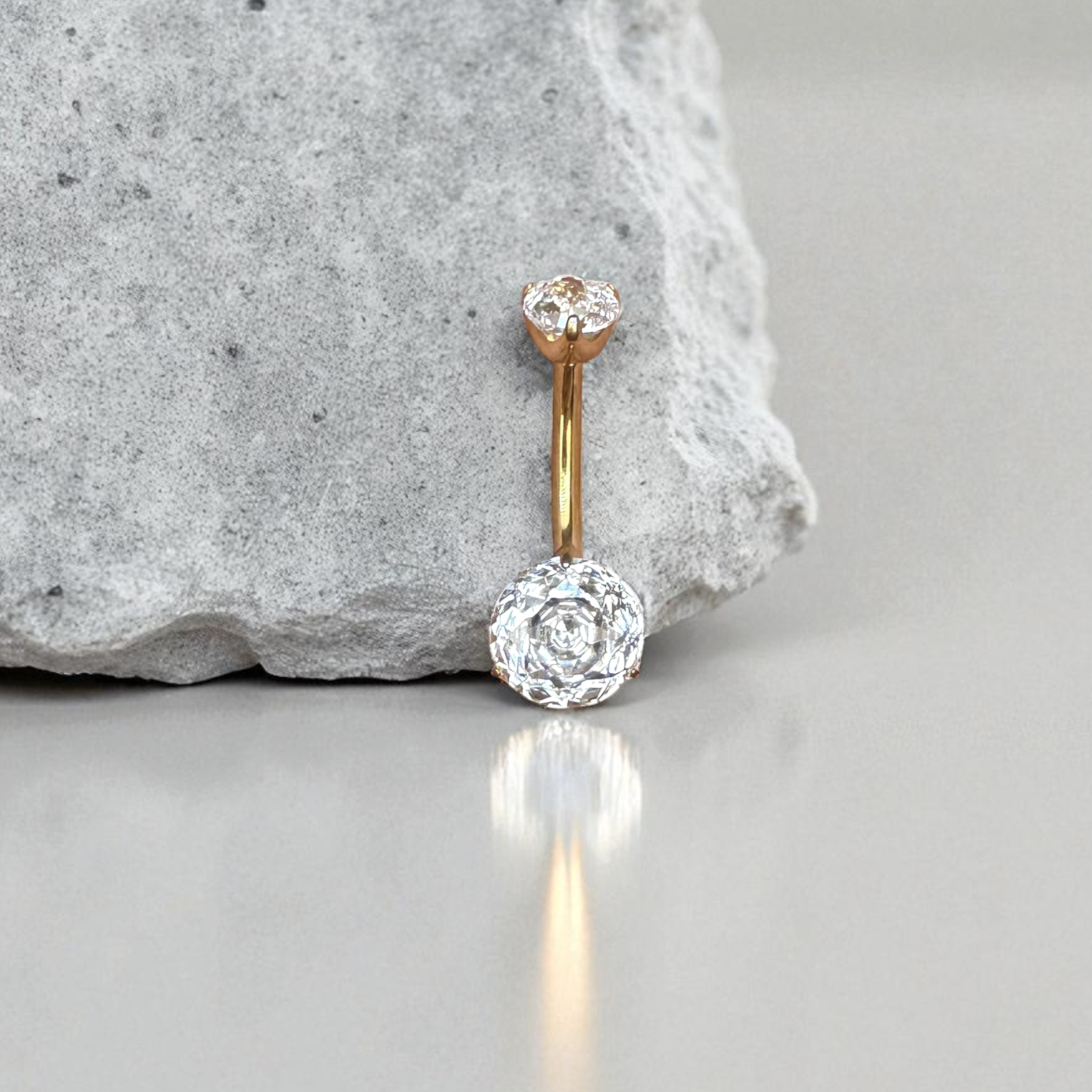 Gold belly button ring with clear gemstone on a gray surface