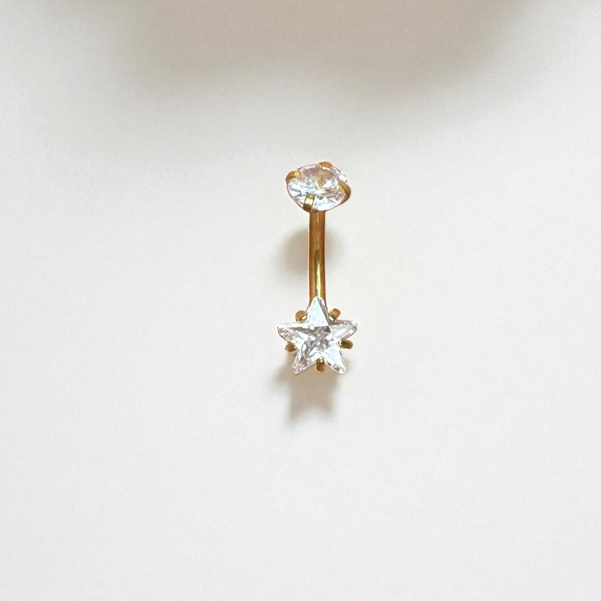 Gold belly button ring with a clear star CZ on a white background