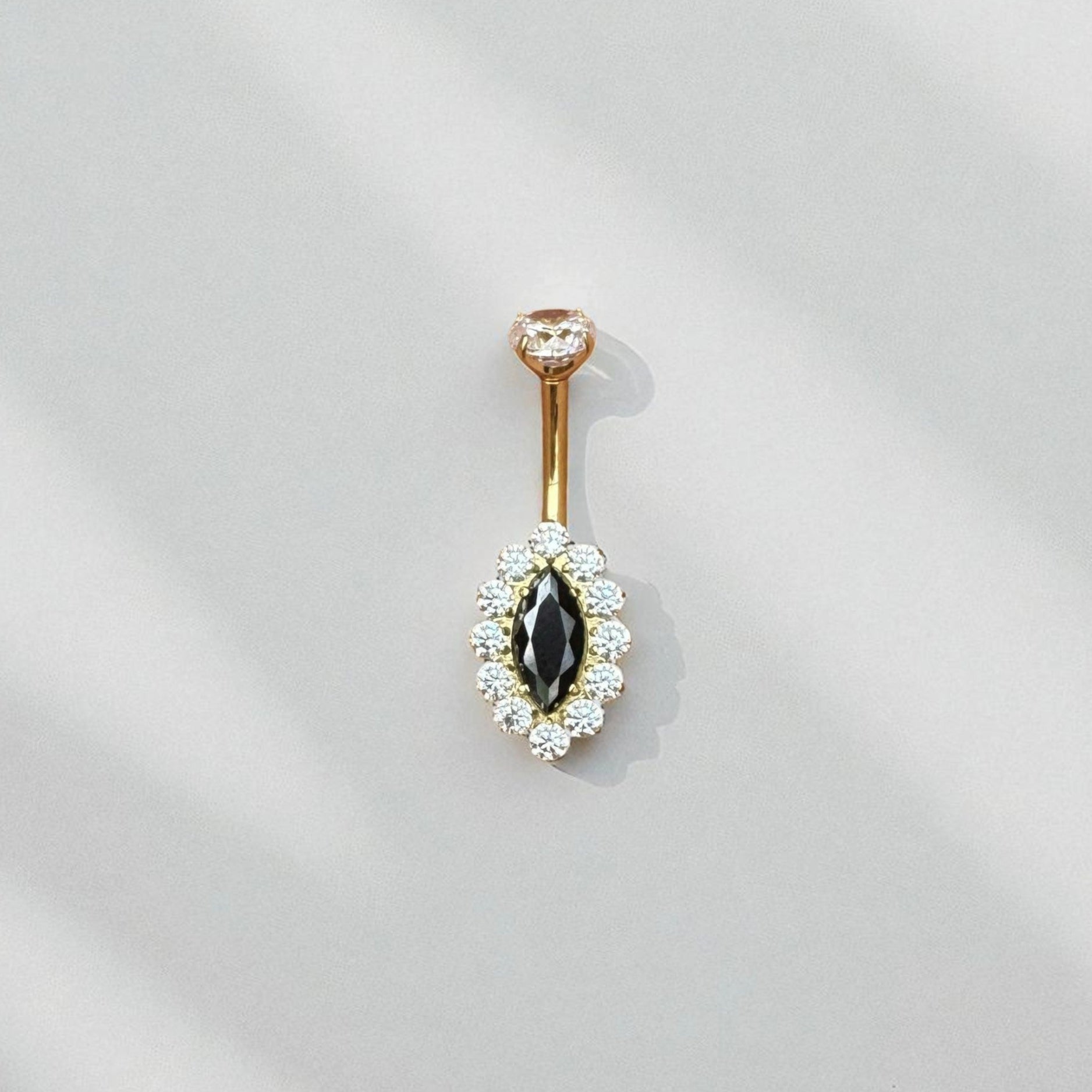 Gold belly button ring with black gemstone and white stones on a light gray background