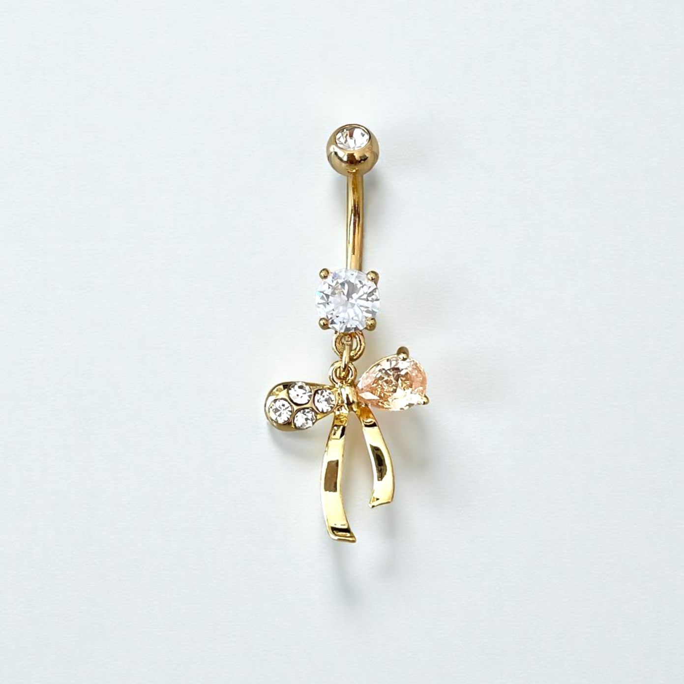 Gold belly button ring with bow and gemstone details on a light gray background
