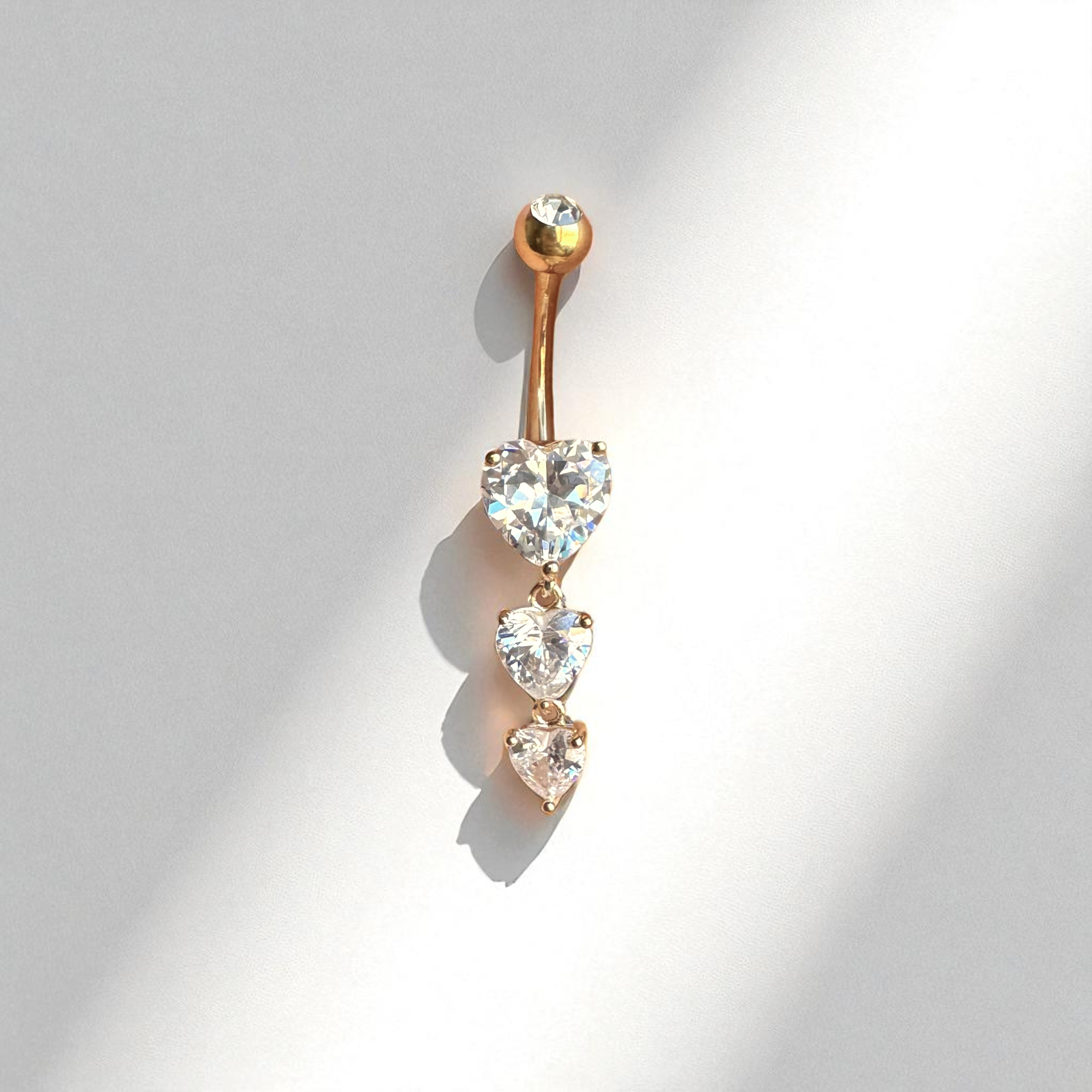 gold belly button ring with heart-shaped gemstones on a light gray background