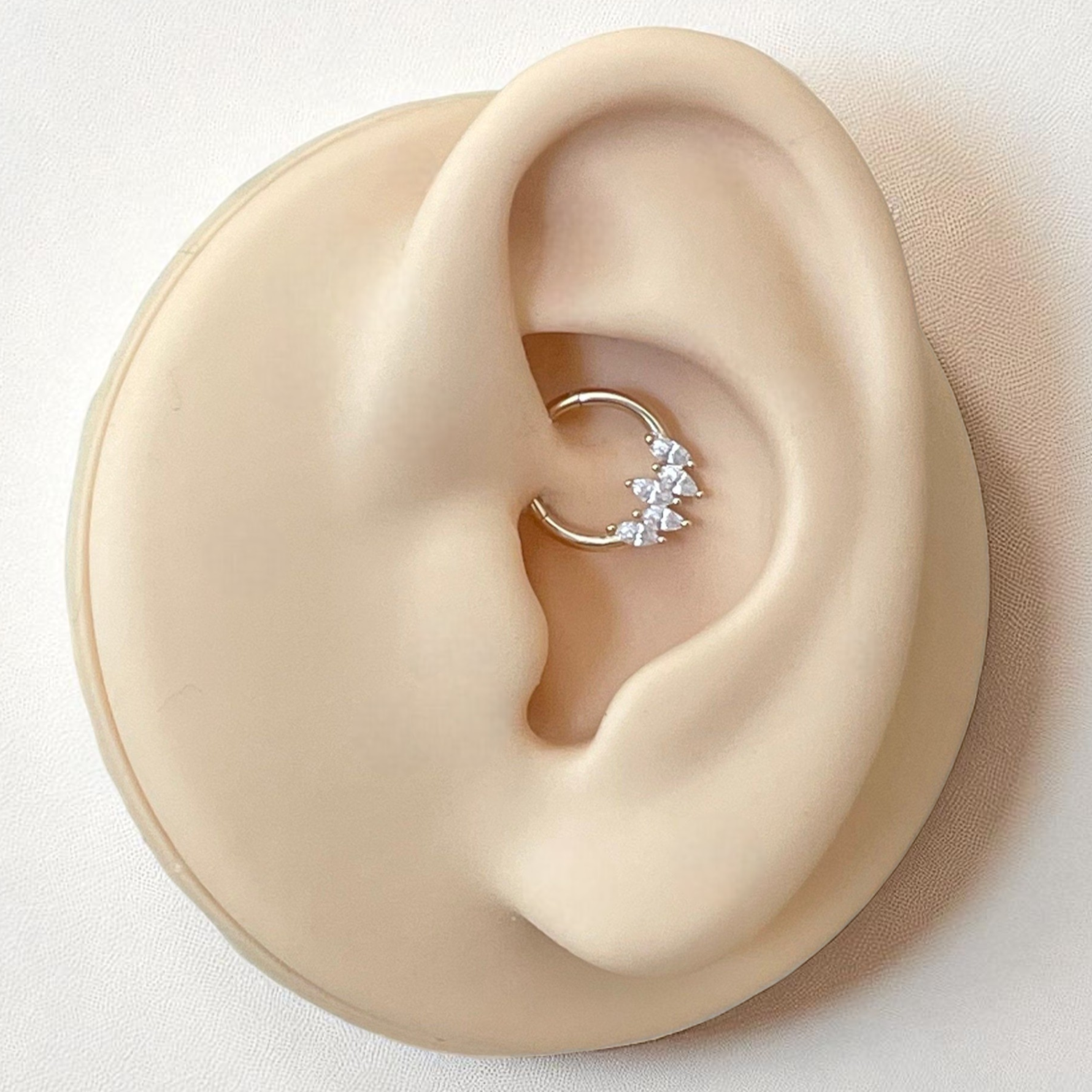 Close-up of an ear wearing a delicate gold and clear crystal daith earring on a neutral background