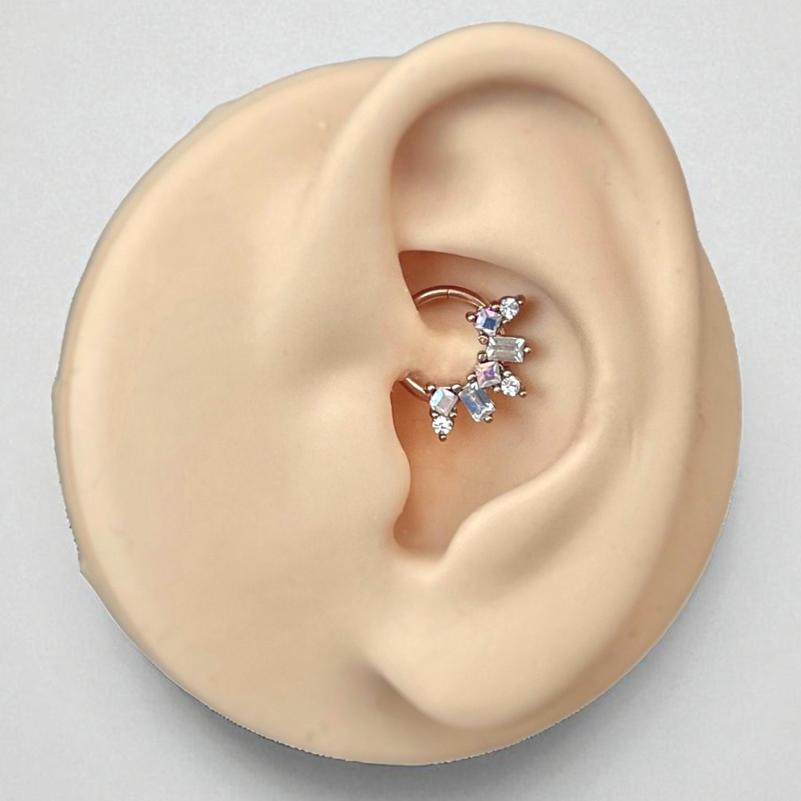 Close-up of an ear wearing a rose gold daith earring on a light gray background