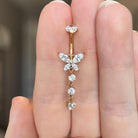 Gold belly button ring with butterfly design held between fingers