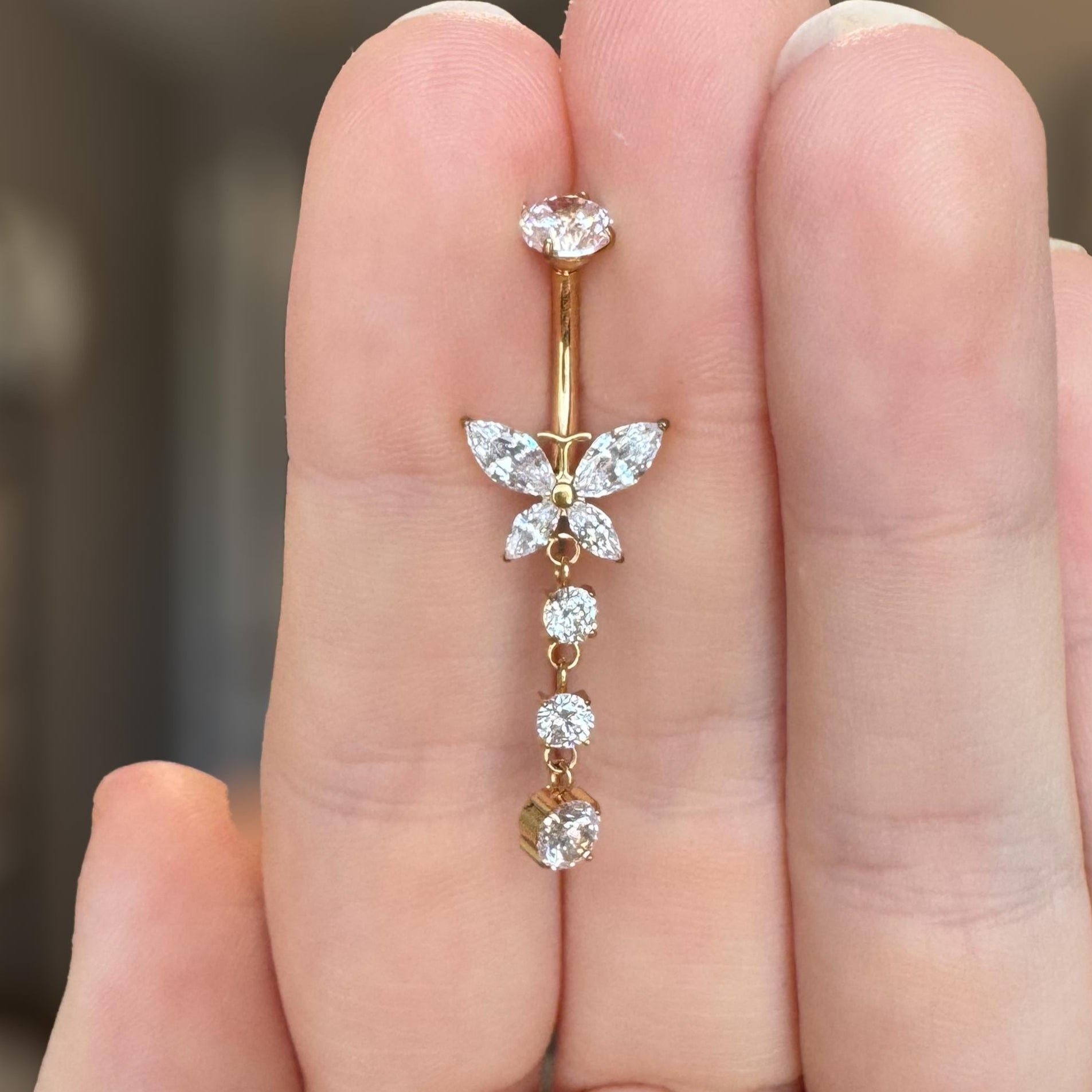 Gold belly button ring with butterfly design held between fingers