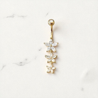 Gold belly button ring with flower-shaped gemstones on a white marble background