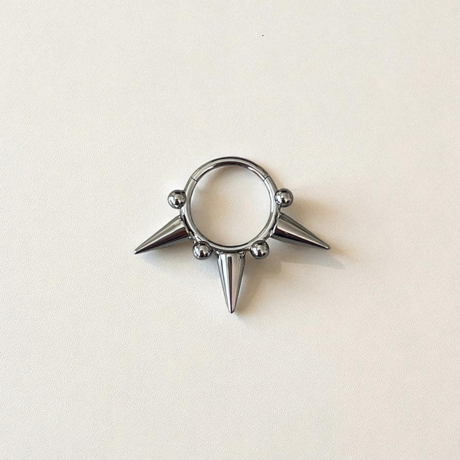 Silver ring with spike design on a beige background