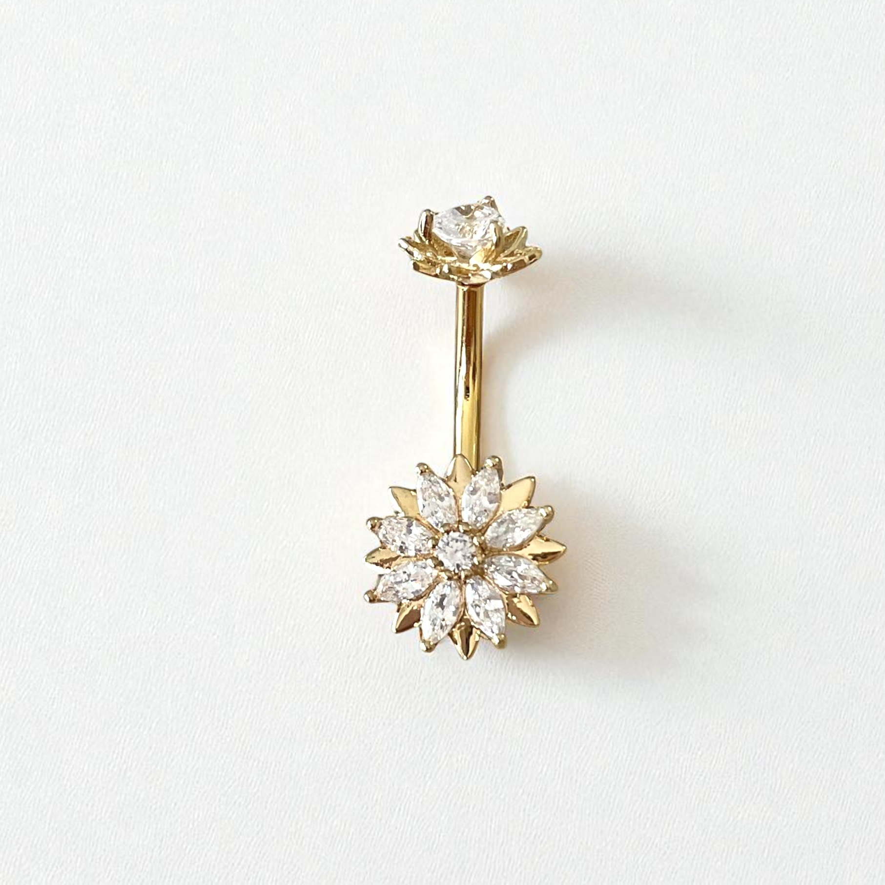 Gold belly button ring with  a flower clear gem centerpiece on a white background