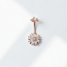 Rose gold belly button ring with clear gemstones in a flower design
 on a white background